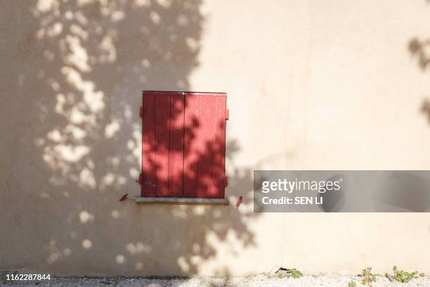 a house with red wooden window in the street with sunlight and tree shadow on wall, gordes, france - provence alpes côte d'azur photos et images de collection
