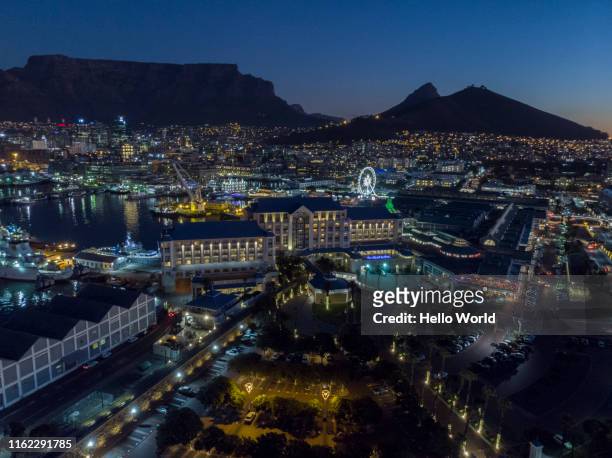aerial shot of city with mountain in the background and ferris wheel lit at night - cape town cityscape stock pictures, royalty-free photos & images