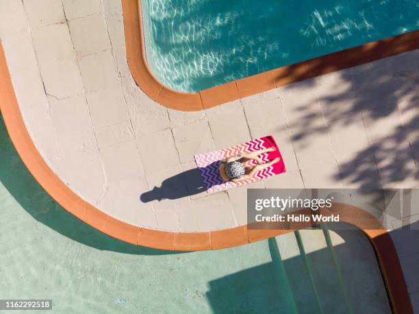 Aerial shot of a young woman seated sunbathing at poolside between two swimming pools