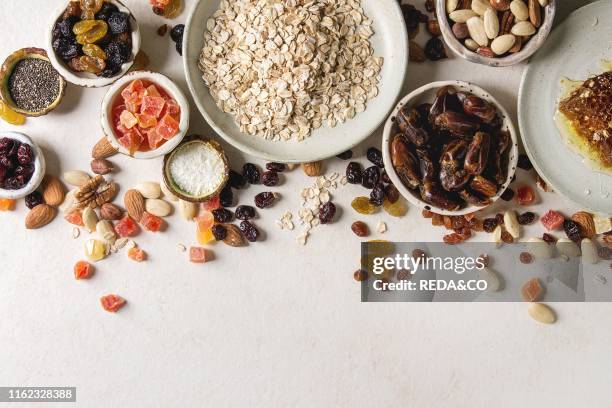 Variety of dried fruits. Nuts. Honey and oat flakes in ceramic bowls for cooking homemade healthy breakfast muesli or granola energy bars over white...