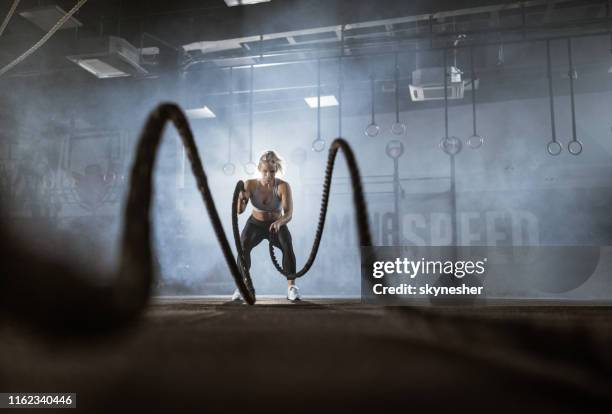 glückliche sportlerin trainiert mit kampfseilen in einem fitnessstudio. - cross fit stock-fotos und bilder