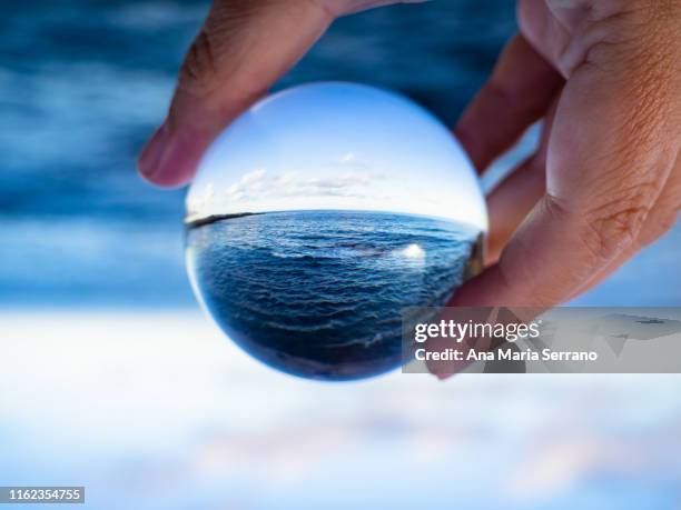 a person with a crystal ball in his hand with the reflection of the sea - glass sphere stock pictures, royalty-free photos & images