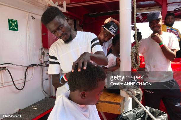 Migrants watch as migrant and barber Abdulmoniem Ahmed from Darfour shaves the head of another young migrant on deck of the 'Ocean Viking' rescue...