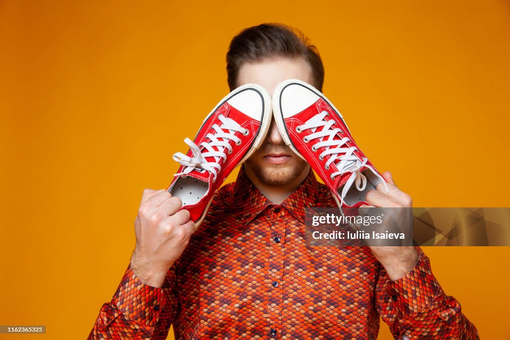 Trendy man covering eyes with red sneakers