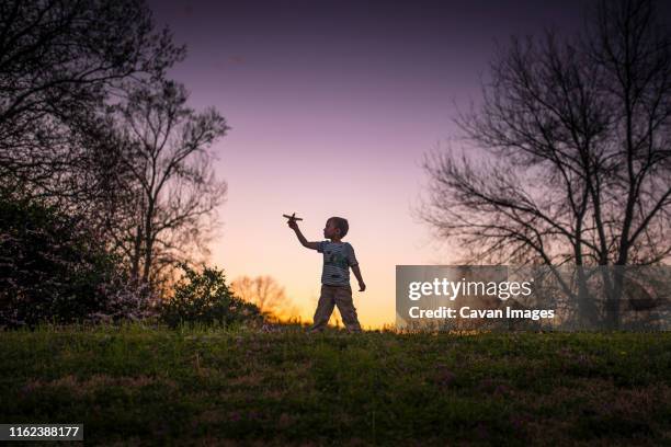 little boy silohette playing w/ an airplane and sunset behind w/ trees - silohette stock pictures, royalty-free photos & images