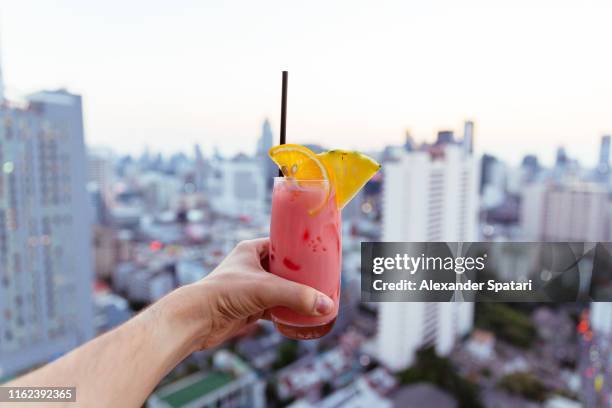 drinking cocktail at the rooftop bar with city view, personal perspective view - cocktail and mocktail stockfoto's en -beelden