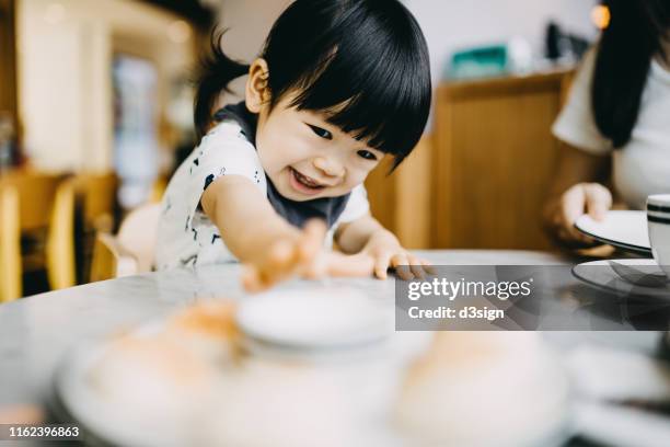 hungry little toddler girl reaching for bread in a restaurant - asian baby eating fotografías e imágenes de stock