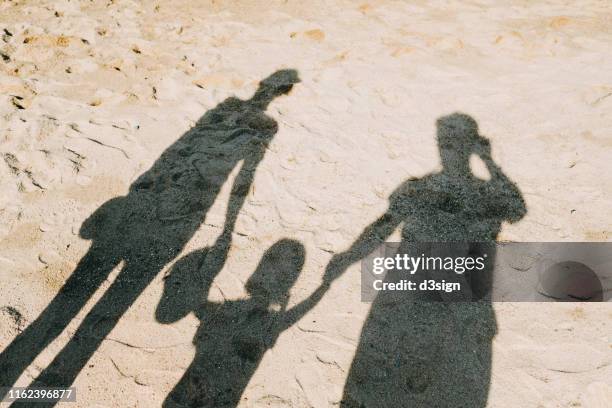 shadow on sandy beach of a loving family of three holding hands relaxing on a lovely sunny day - vater mutter kind stock-fotos und bilder