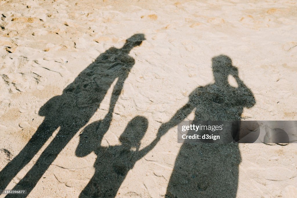 Shadow on sandy beach of a loving family of three holding hands relaxing on a lovely sunny day