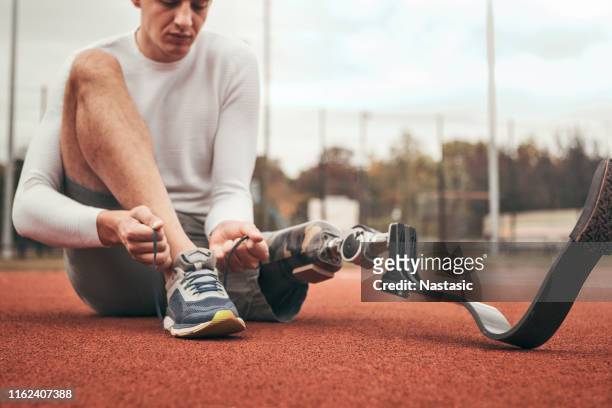 junger mann mit prothesenbein binden seine schuh schnürsenkel vor dem sporttraining - laufwettbewerb der männer stock-fotos und bilder