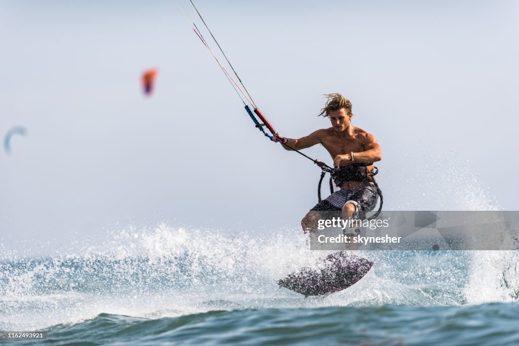 Athletic man having fun while kitesurfing on the sea.