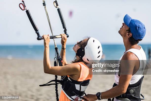 joven instructor preparando a una mujer para kiteboarding en la playa. - kiteboarding fotografías e imágenes de stock