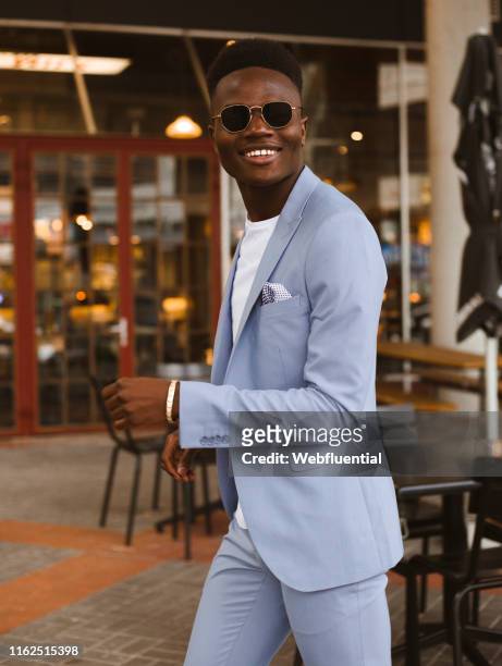 Young black South African man wearing a blue suit and sunglasses indoors