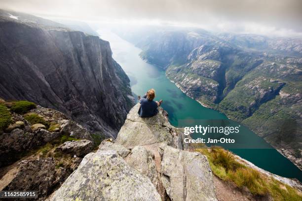 wandelaar zittend op kjeragnasen over lyseford in noorwegen - bergen norway stockfoto's en -beelden