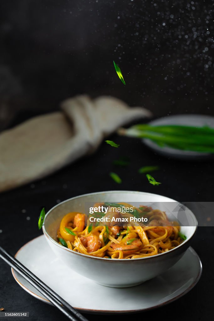 Roergebakken Udon noedels, garnalen, prei en groenten. Aziatisch gezond eten in kom over zwarte achtergrond, kopieer ruimte.