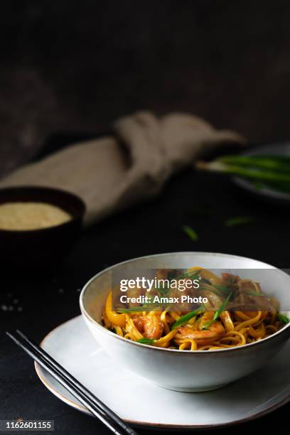 udon stir-fry noodles with shrimp and vegetables on black background in dark and moody style - stirfry stock pictures, royalty-free photos & images