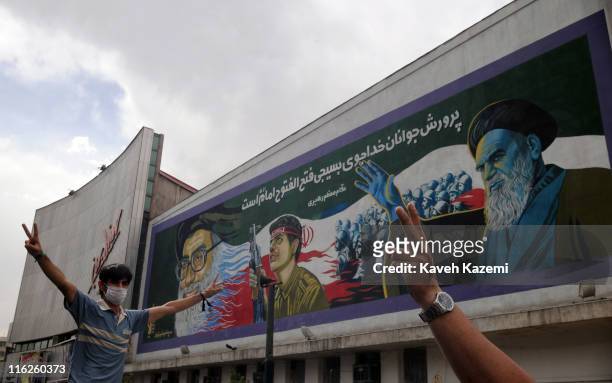 In front of a huge mural of Ayatollah Ali Khamenei and Ayatollah Ruhollah Khomeini, a pro-reforms protestor flashes victory signs on the corner of...