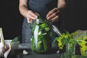 Woman cooking marinated cucumbers with garlic and dill on black. Rustic dark style.