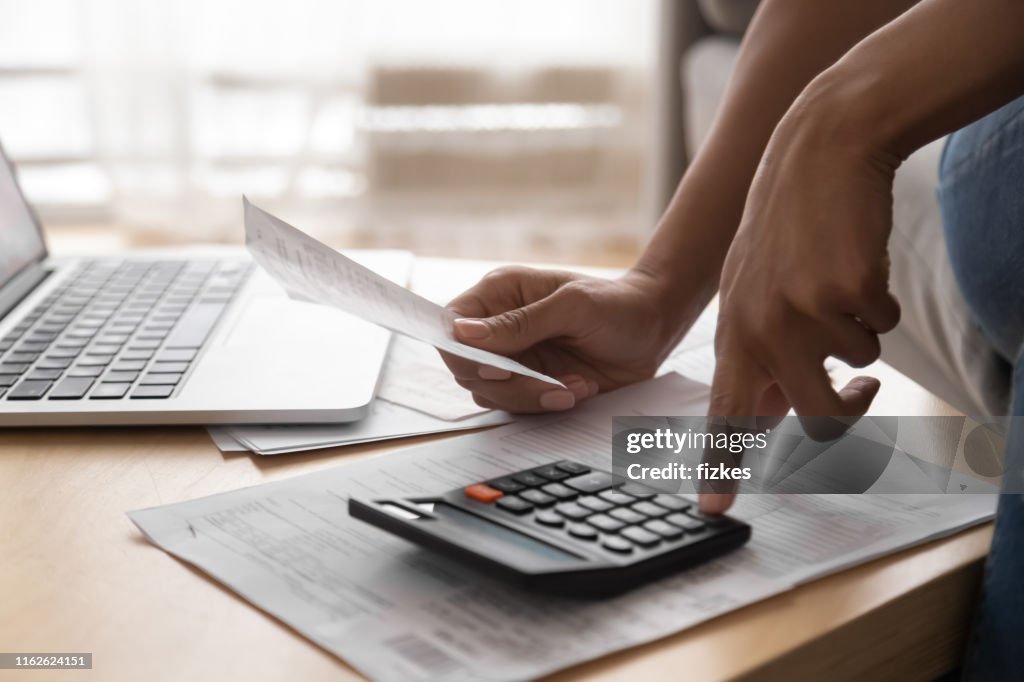 African woman holding paper bills using calculator, close up view