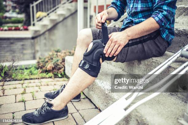 man sitting on the steps and adjusting his orthosis after having knee sprain - orthopaedic equipment stock pictures, royalty-free photos & images