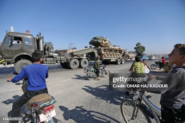 Inhabitants of Maaret al-Numan in Syria's northern province of Idlib watch as a vehicle carries a Turkish tank which part of a convoy of military...