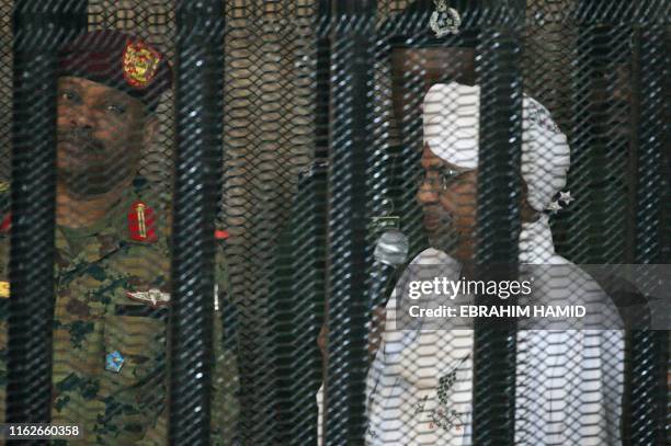 Sudan's deposed military ruler Omar al-Bashir stands in a defendant's cage during the opening of his corruption trial in Khartoum on August 19, 2019....