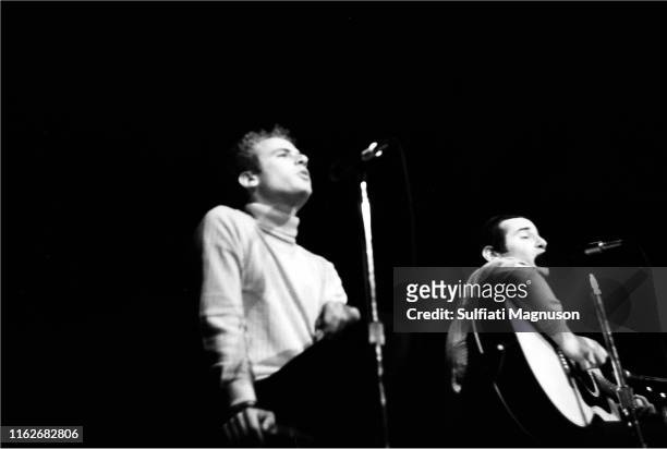 Paul Simon, eyes closed and Art Garfunkle seated and holding the top of the stool with his right hand, as they sing performing on stage at the...