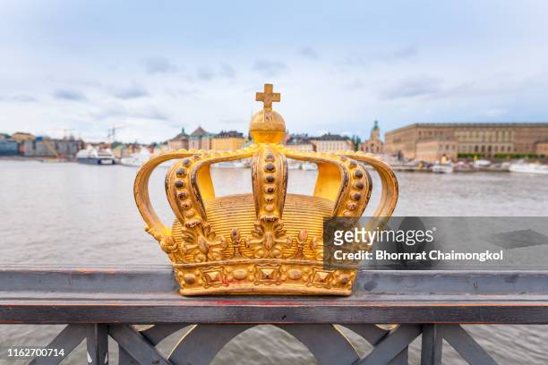 gilded crown at the middle of skeppsholmen bridge with gamla stan in the background at stockholm, sweden - könig königliche persönlichkeit stock-fotos und bilder