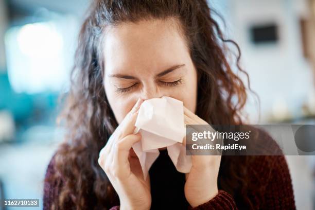 young woman blowing her nose on a tissue - blowing-nose stock pictures, royalty-free photos & images