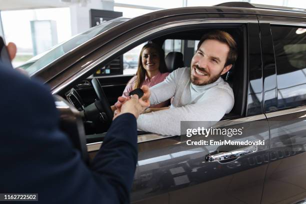 couple receiving a new car keys from car salesperson - contrato de arrendamento imagens e fotografias de stock