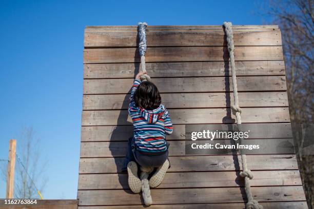 a strong child pulls himself up a rope course on a wooden wall outside - boys in pullups stock-fotos und bilder