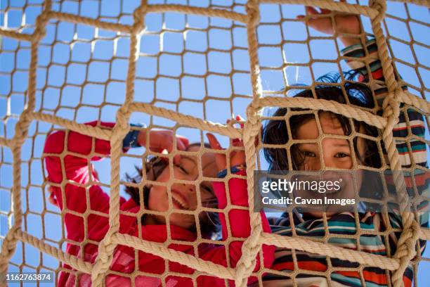 two laughing children peer down through a rope net against blue sky - kid looking up to the sky imagens e fotografias de stock