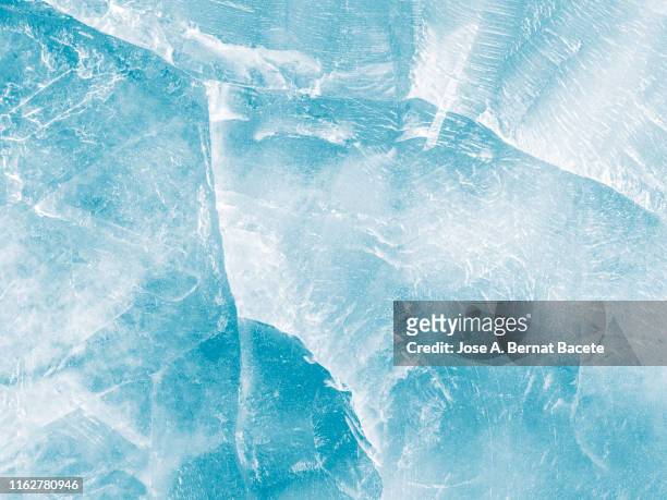 full frame of the textures formed of a block of cracked ice on a soft blue color background. - froid photos et images de collection