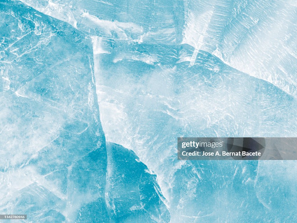 Full frame of the textures formed of a block of cracked ice on a soft blue color background.