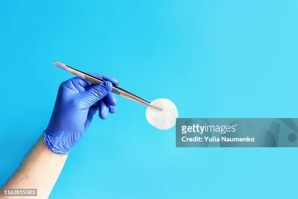 medicine and surgery theme: doctor's hand in a blue glove holding a pair of tweezers with a cotton pad on a blue background, isolated. - pince chirurgicale photos et images de collection