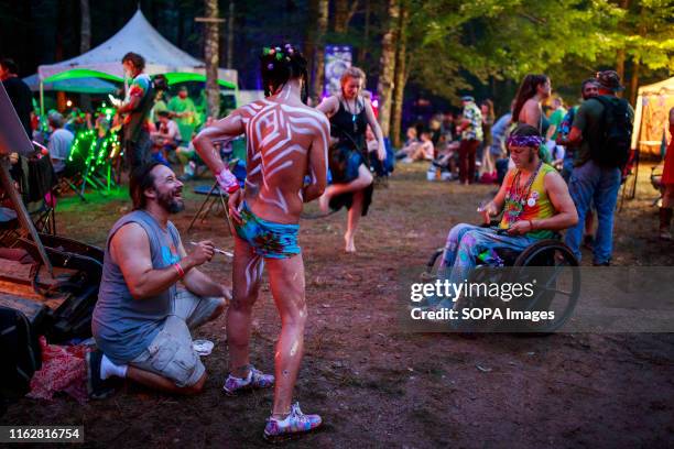 Body paint artist puts finishing touches on the arm of a topless woman during the Yasgur Road Reunion at Max Yasgur's farm during 50th Anniversary of...