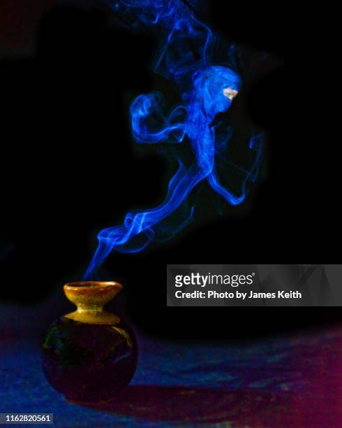 a bottle emits blue smoke which takes the form of a genie. - djinn stockfoto's en -beelden