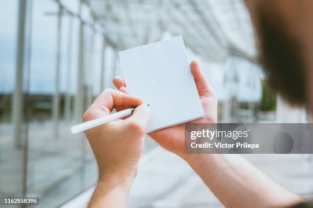 mock up notebook in a man's hand, against the background of a glass building. - topnews stock pictures, royalty-free photos & images