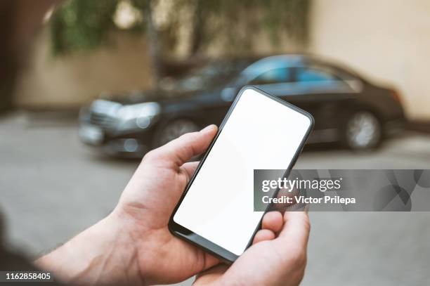 mock up smartphone in man's hand, in the background a black car. - car display background stock-fotos und bilder