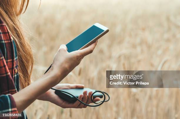 girl in a yellow field holding a phone in her hand, and charging it from power bank. - powerbank stock-fotos und bilder