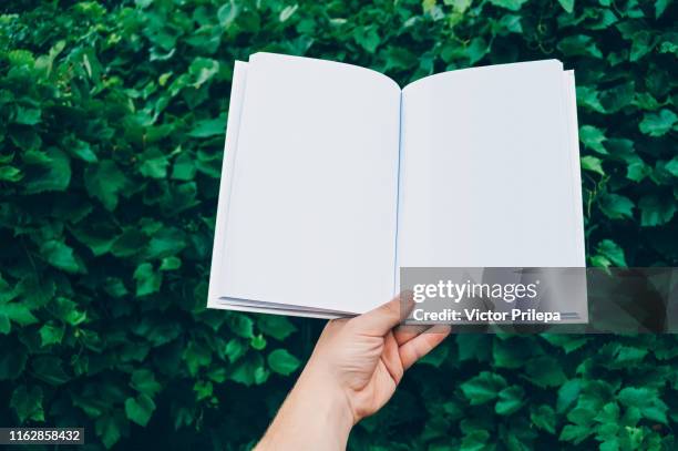 mock up of the book in hand man, against the background of green leaves. concept on the topic of education - back to school. - mockup print stockfoto's en -beelden