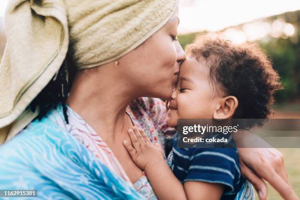 junge afrikanische nachkommen mutter küsst ihren kleinen sohn auf der stirn - mutter baby stock-fotos und bilder