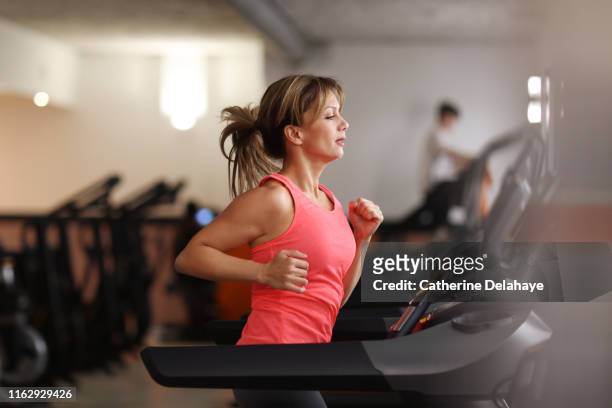 woman running on treadmill at fitness center - women working out gym stock pictures, royalty-free photos & images