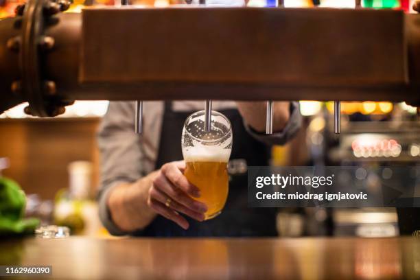 unkenntlich barista gießt ein bier in einer kneipe - bier zapfhahn stock-fotos und bilder