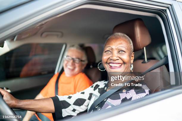 porträt einer seniorin, die ein auto fährt, und einer freundin auf dem beifahrersitz - female driving stock-fotos und bilder