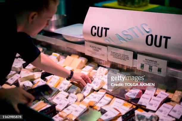 Member of staff arranges cheese in cellulose plastic-free packaging for sale at Budgens supermarket in Belsize Park, north London on July 2, 2019. -...