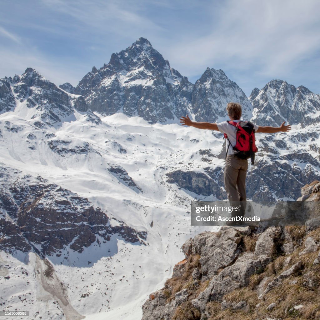 Hiker stands on cliff top with arms out
