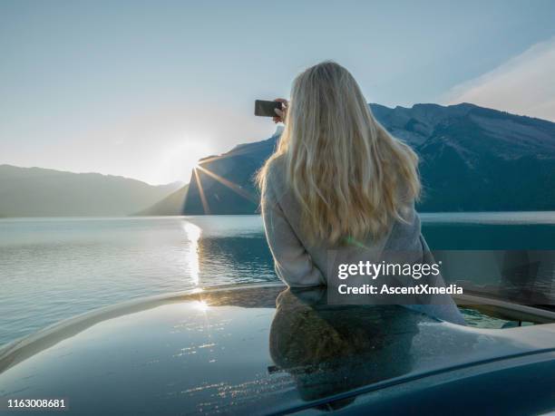 woman takes photo with cell phone from car sunroof - car appearance stock pictures, royalty-free photos & images