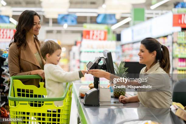 lindo niño entregando una tarjeta de fidelización a la caja registradora antes de escanear productos en la caja en un supermercado - superalmacén fotografías e imágenes de stock