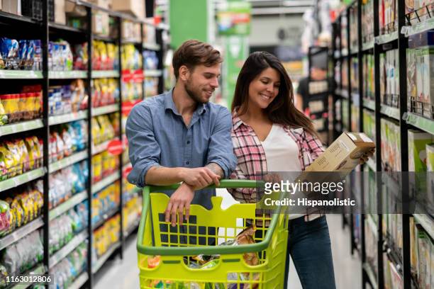 mooie vrouw het tonen van een graan doos aan mannelijke partner terwijl hij duwt de kar in de supermarkt - cereal box stockfoto's en -beelden